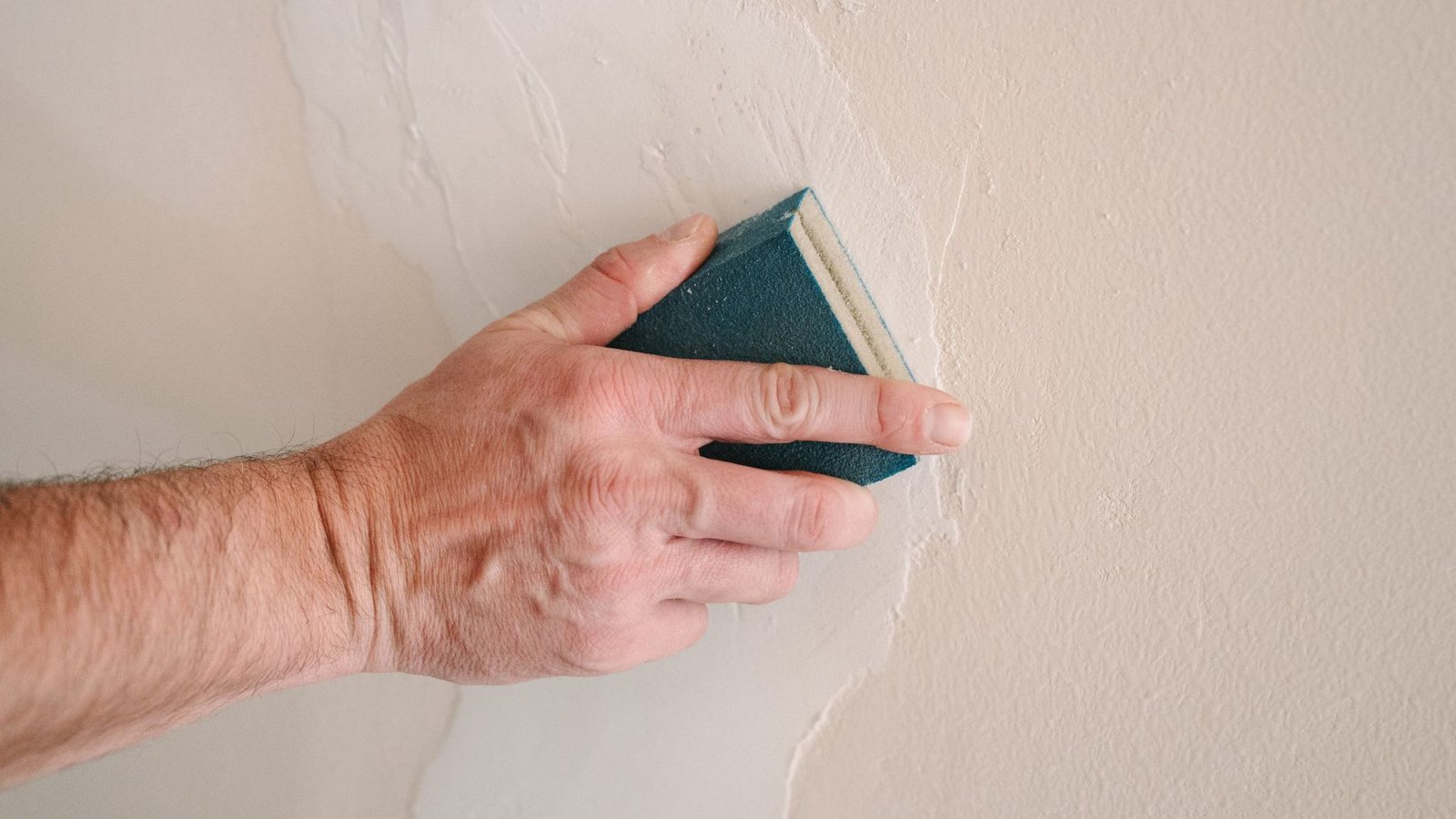 Hand sanding patched basement wall surface smooth during crack repair to prep for waterproofing.