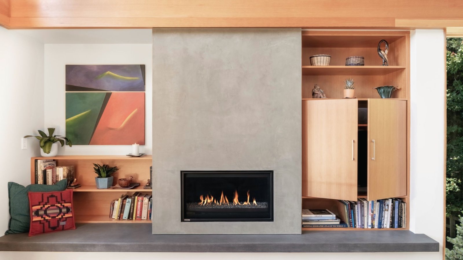 Modern basement gas fireplace set in concrete wall with built-in shelves and abstract art.